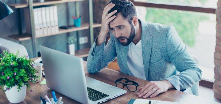 Man holding his head in sadness looking at his laptop
